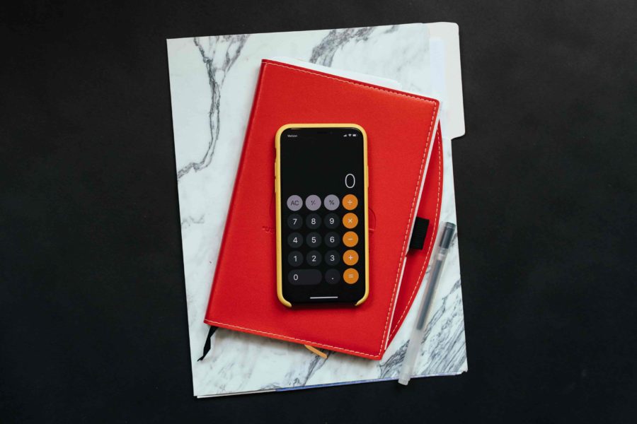 Mobile phone with calculator app open sitting on notebook and ipad on desk