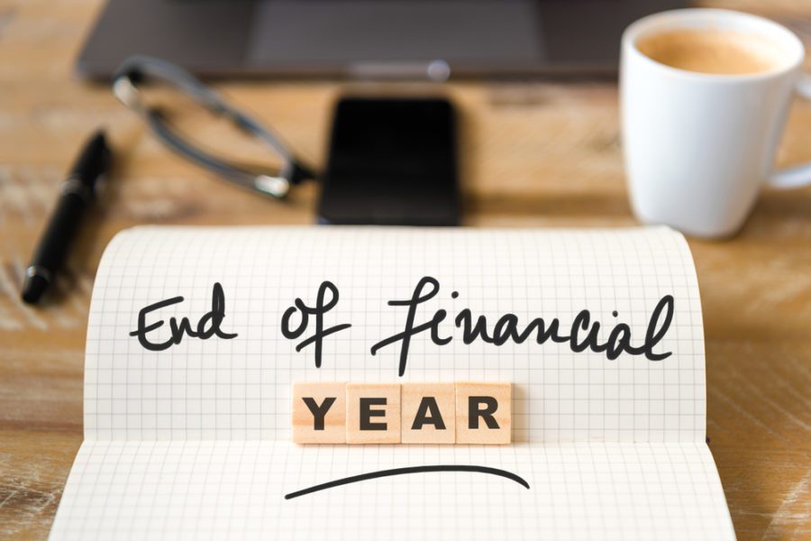 Closeup on notebook over wood table background, focus on wooden blocks with letters making End of Financial Year text.