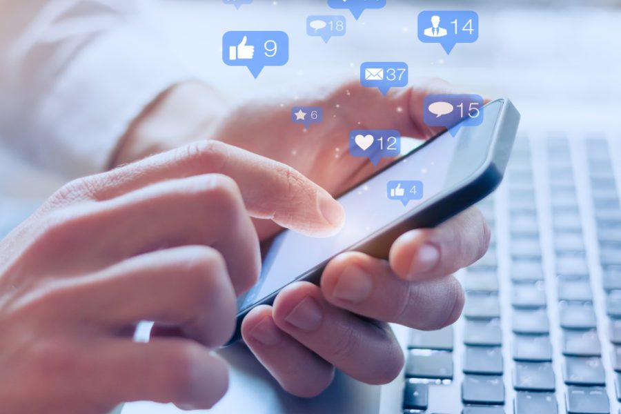 Social media interactions on mobile phone, concept with notification icons of like, message, email, comment and star above smartphone screen, person hands holding device.