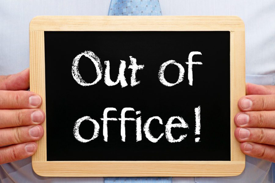 A business owner holding a chalk board with the words Out of Office!